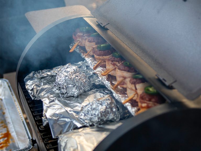 Open smoker shows smoke cooking chamber filled with food and smoke billowing out.