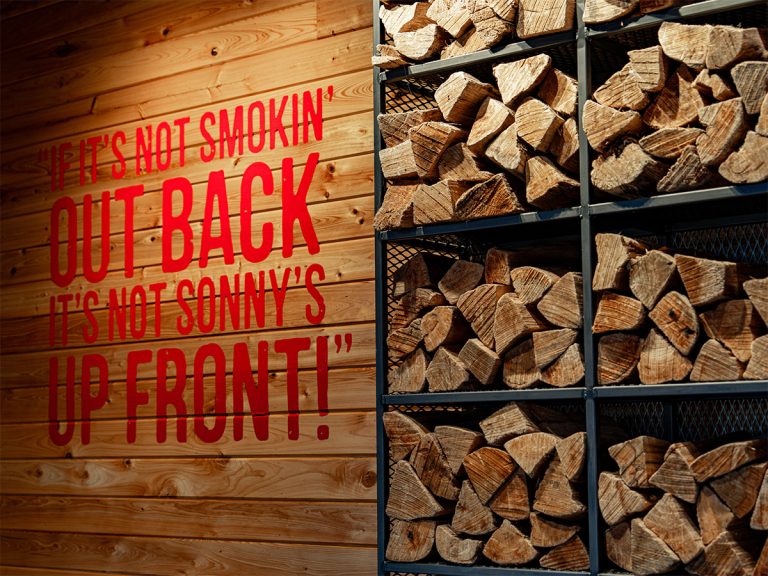 stacks of oak wood next to sign at Sonny's BBQ reading "If it's not smokin' out back, it's not Sonny's up front!"