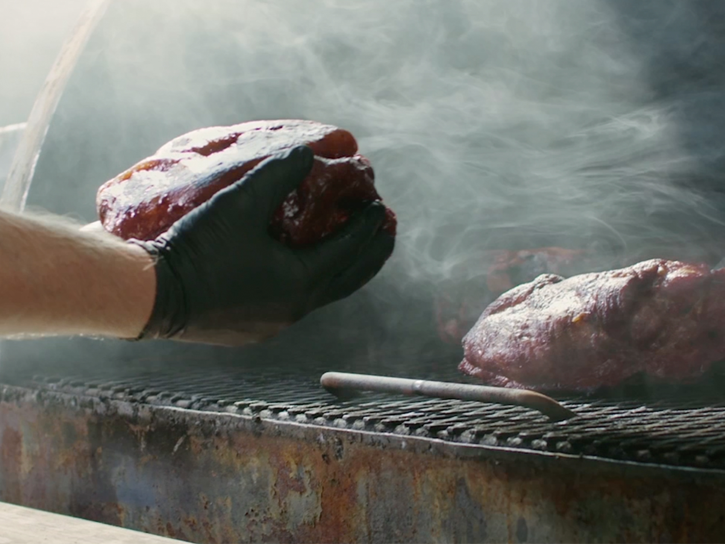 Pitmaster grabs pork butt from smoker.