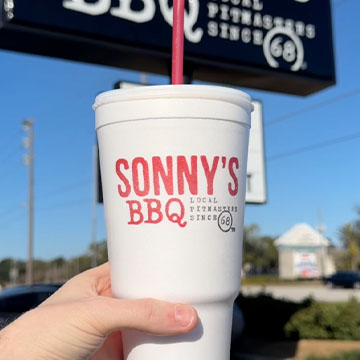 Hand holds cup in front of Sonny's sign