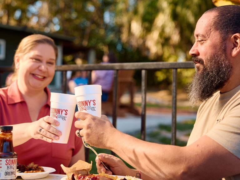 Man and woman cheers cups at table.