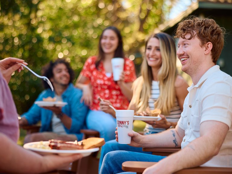 Guests sit in lounge chairs with plates of food and Sonny's BBQ cups