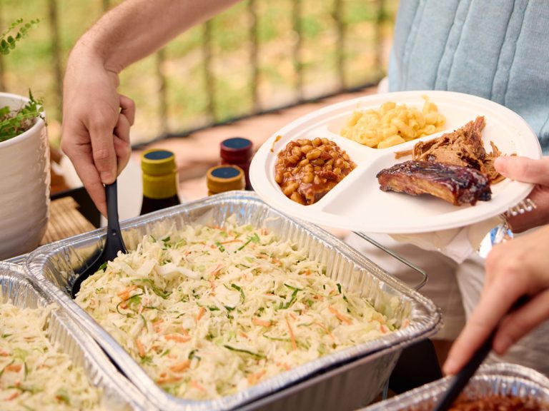 Young man grabs spoon from tray of coleslaw for his plate.