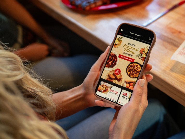 Woman holds phone showing home screen of Sonny's BBQ App