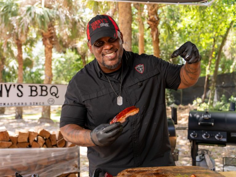 Man poses and smiles while pointing at St. Louis Rib he's holding