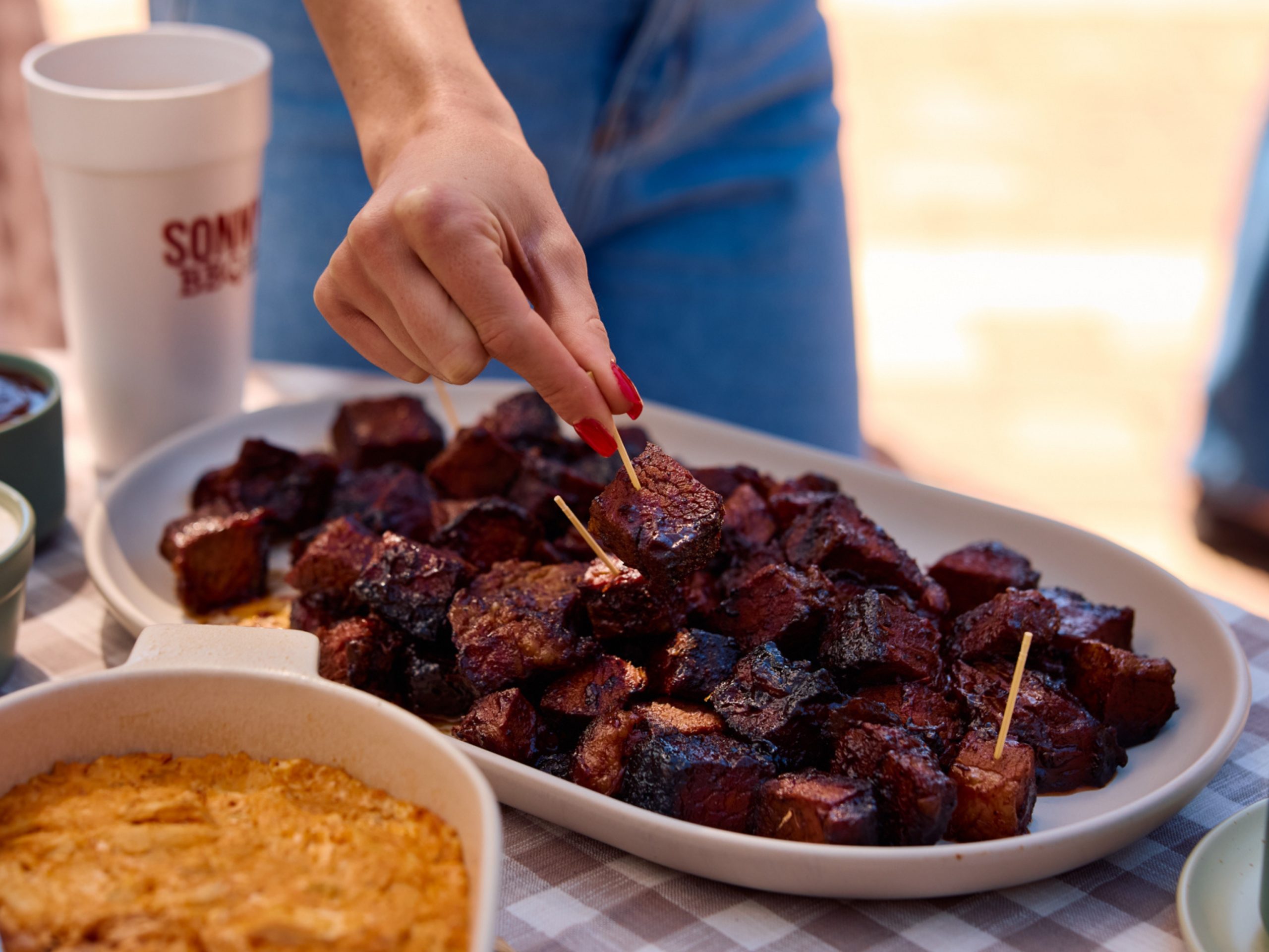 Woman grabs burnt ends by toothpick from platter
