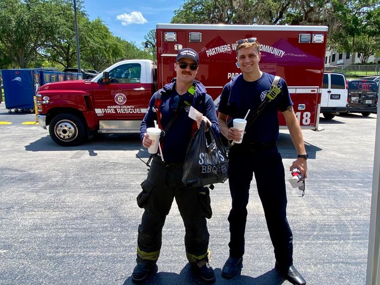 Two first responders with marion County Fire Rescue smile while holding Sonny's BBQ bags